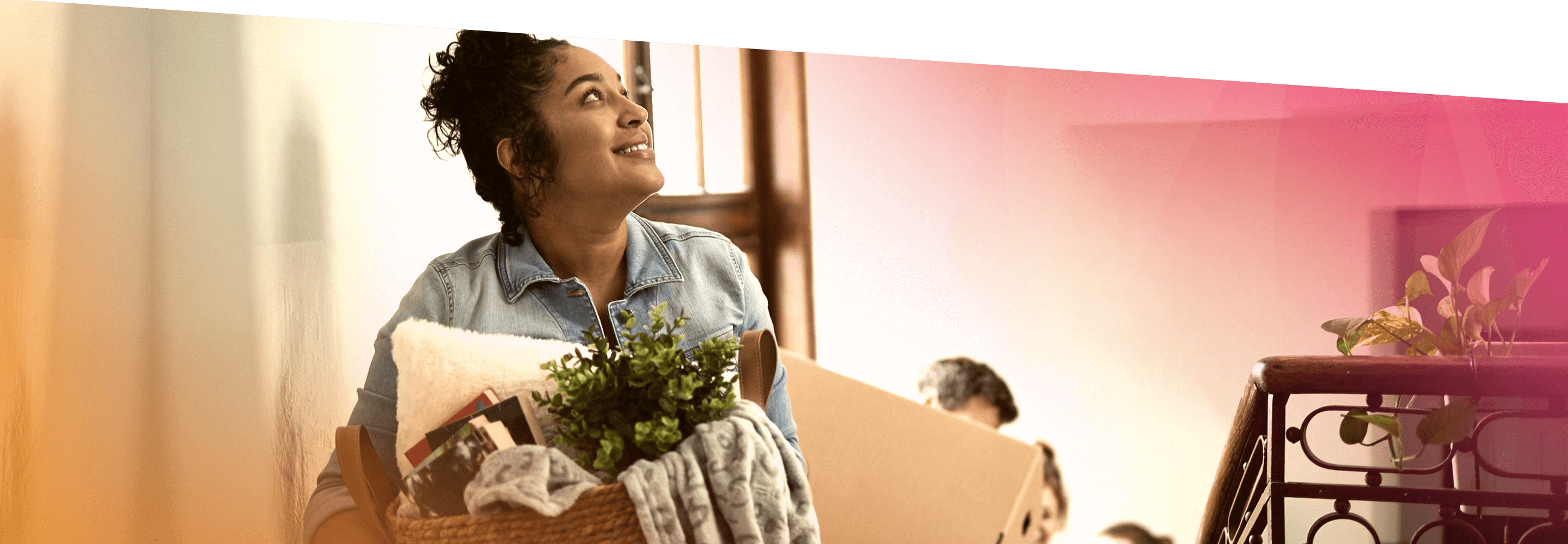 A woman moving into her new home looks happy as she carries a laundry basket full of household items up the stairs